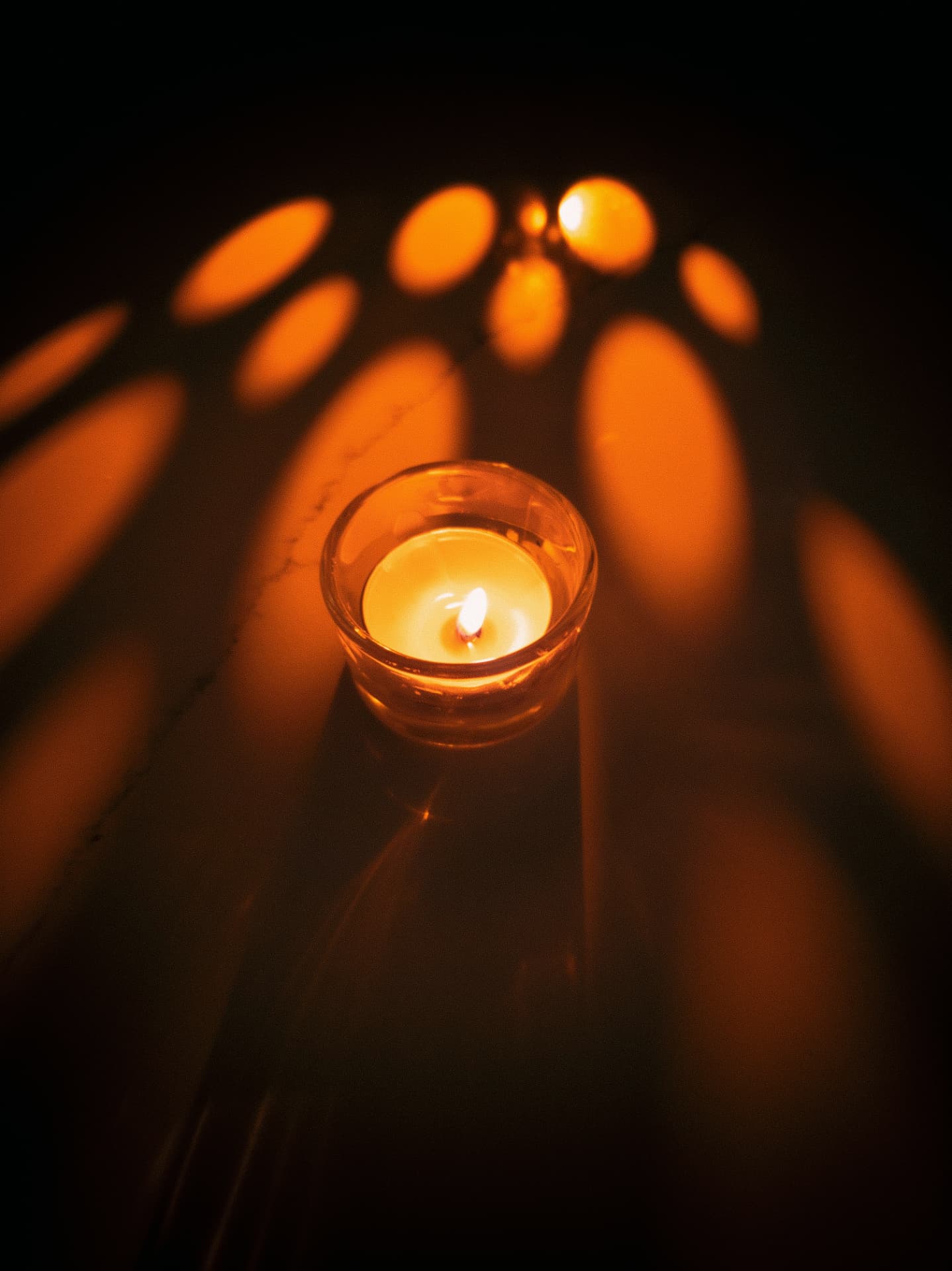 A single glass tealight casting warm oval patterns of light in a dark room